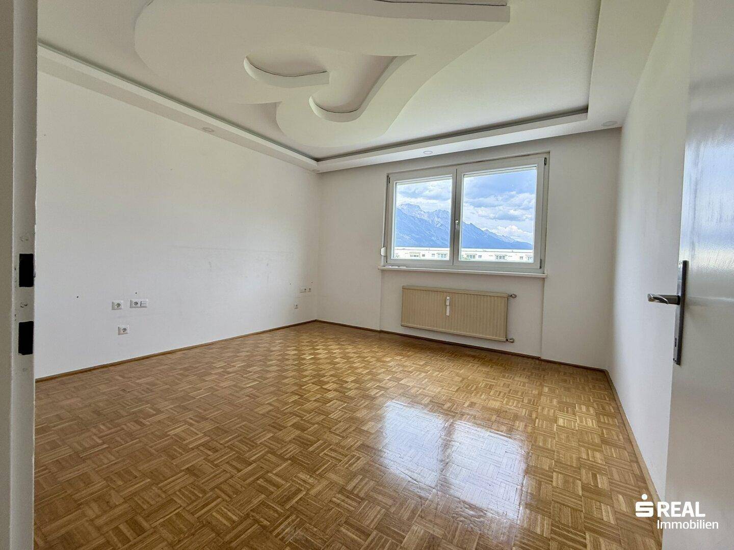 Helles Zimmer mit Parkettboden, dekorativer Decke und weitem Blick auf die umliegende Berglandschaft.