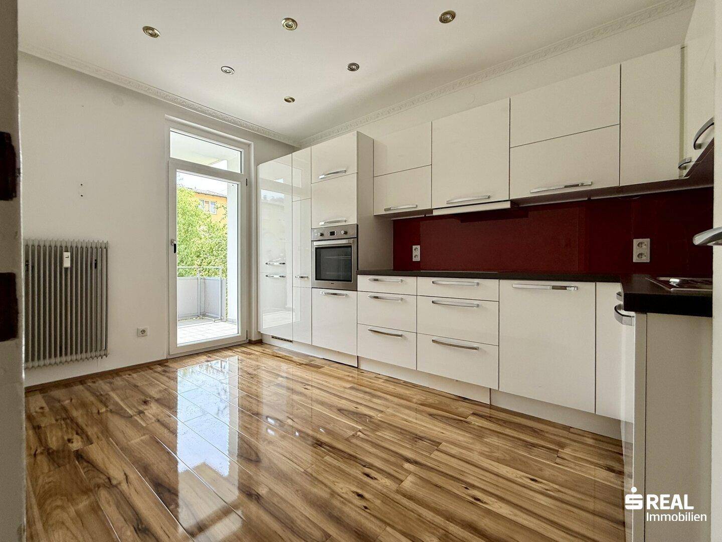 Moderne Einbauküche mit weißen Hochglanzfronten, integriertem Backofen und Zugang zum Balkon.