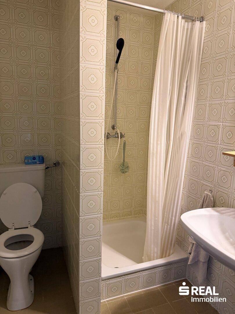 Funktionales Badezimmer mit gemusterten Fliesen, Toilette, Waschbecken und einer Duschkabine mit Vorhang.