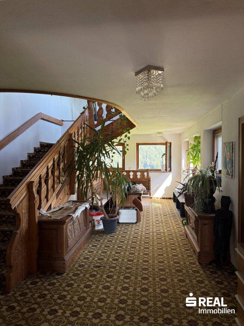 Geräumiger Flur mit einer kunstvoll geschnitzten Holztreppe, gemustertem Teppich und viel Tageslicht.