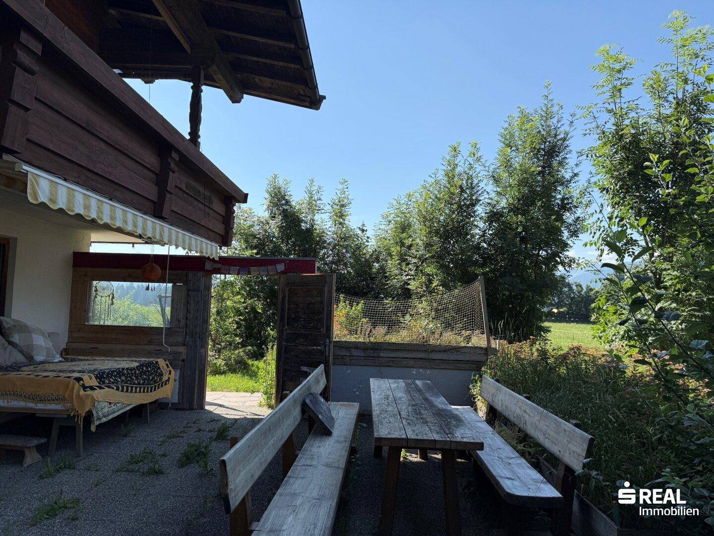 Rustikale Terrasse mit Holzbänken und Tisch, umgeben von Bäumen und Natur, ideal für Mahlzeiten im Freien.