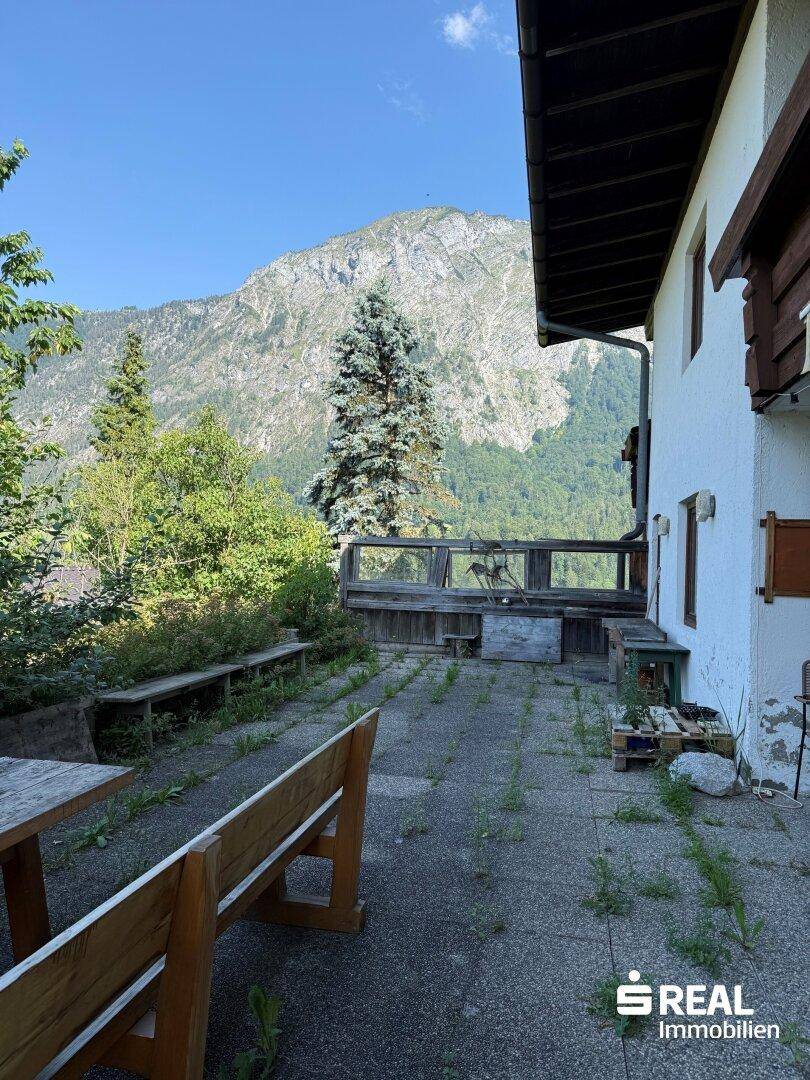 Große gepflasterte Terrasse mit Holzbänken und beeindruckendem Bergblick, ideal für Entspannung im Freien.