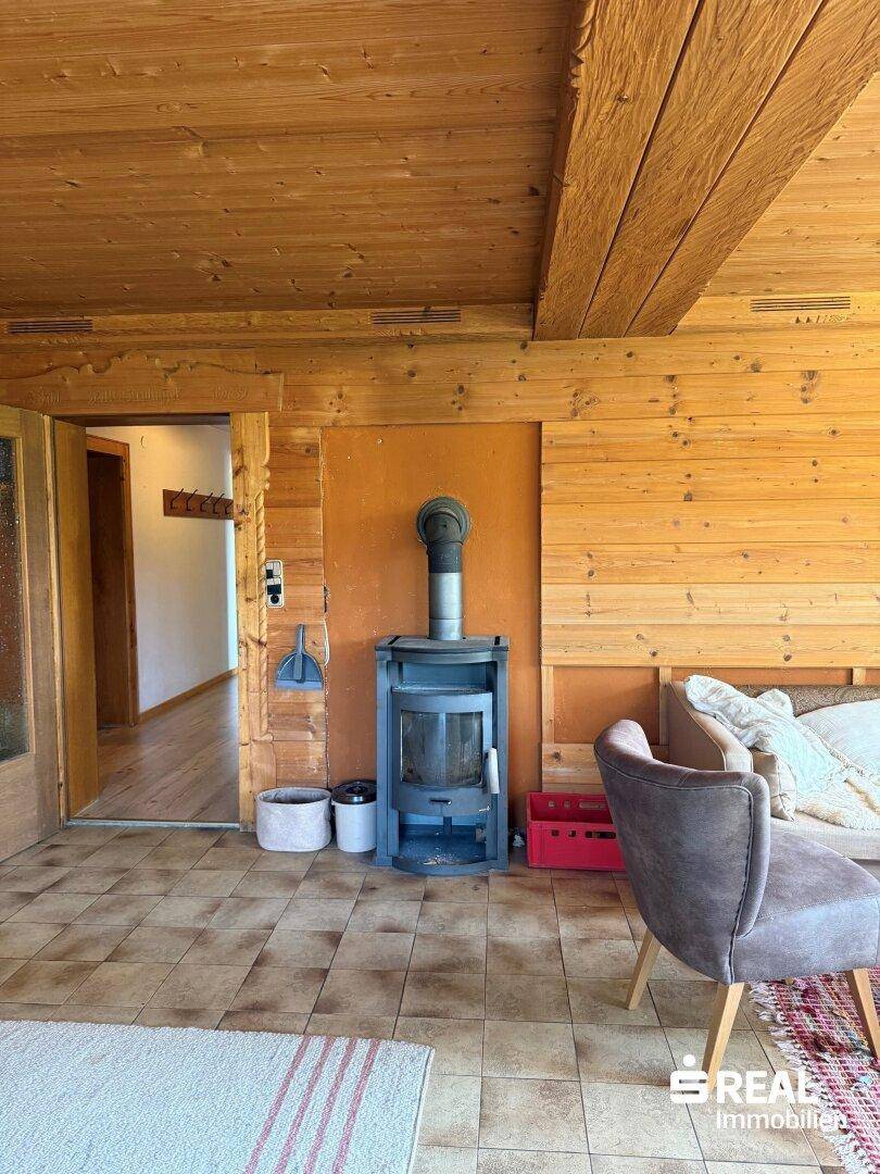 Gemütlicher Wohnbereich mit Holzwänden, Holzbalkendecke und einem modernen Holzofen als Wärmequelle.
