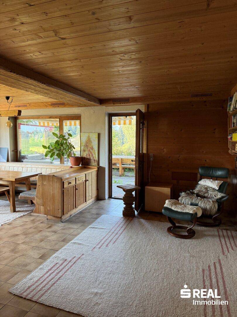 Geräumiger Wohn-Essbereich mit Holzelementen, Fliesenboden und Zugang zu einem Außenbereich.