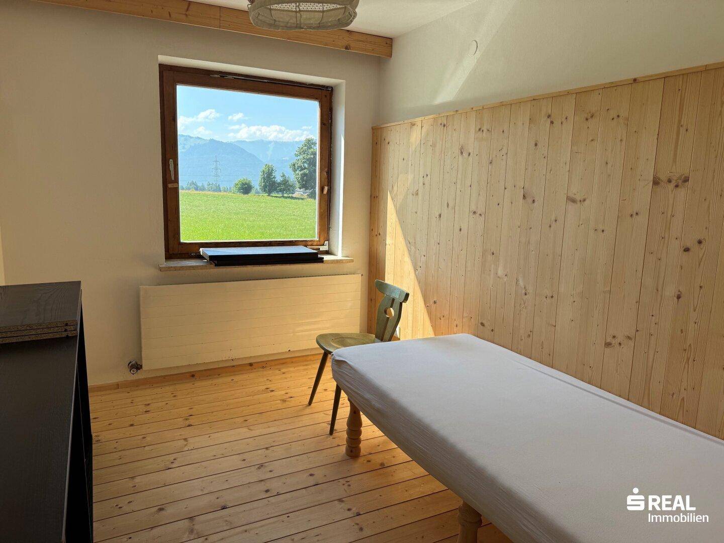 Helles Zimmer mit Holzwänden und Holzboden, bietet einen weiten Blick auf die grüne Landschaft und Berge.