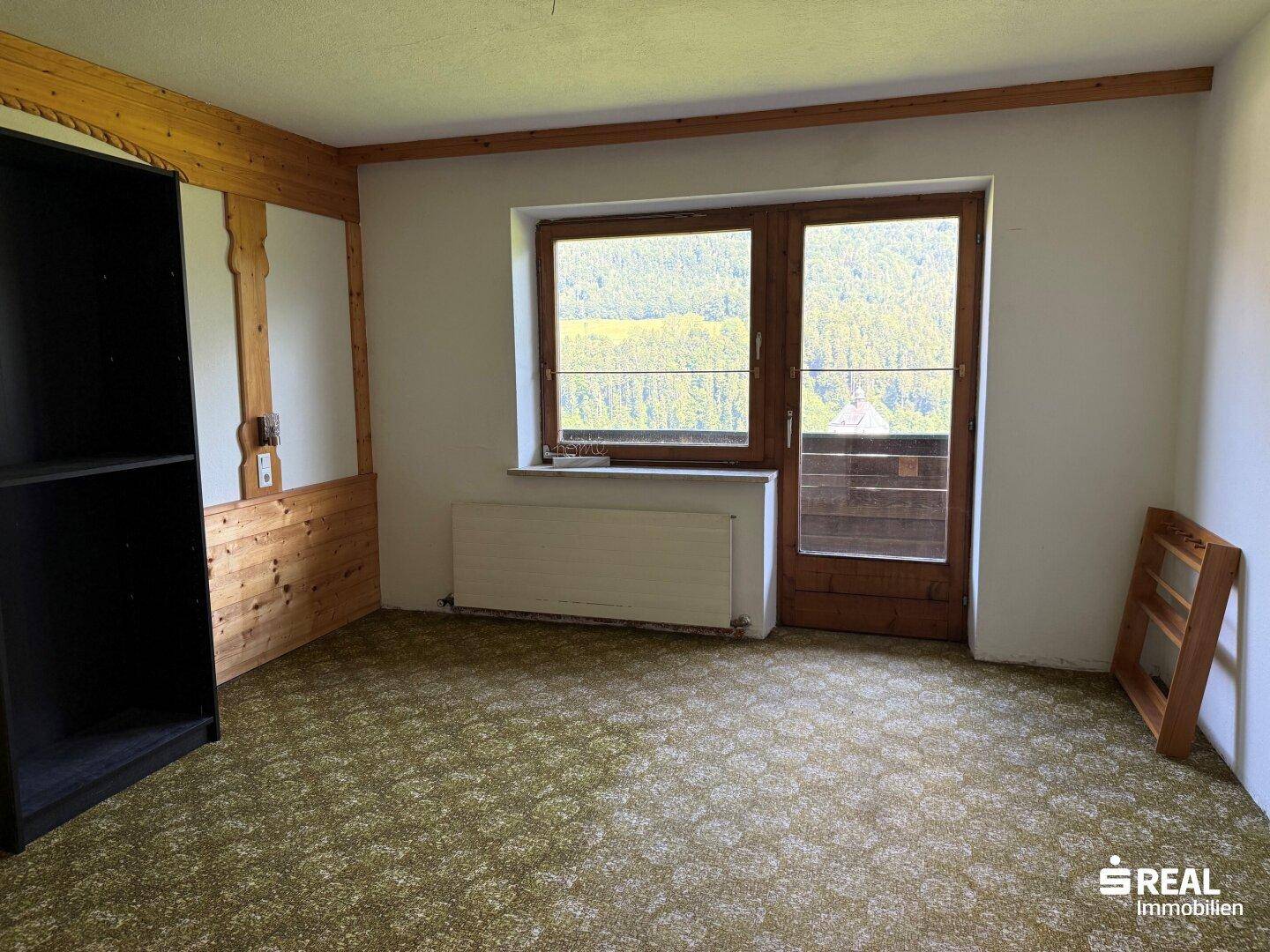 Gemütliches Zimmer mit Holzwänden, Teppichboden und Zugang zu einem Balkon oder einer Terrasse.
