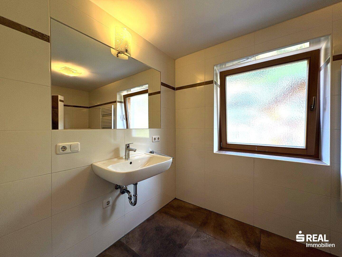 Helles Badezimmer mit Waschbecken, großem Spiegel und einem Fenster für natürliche Belüftung.