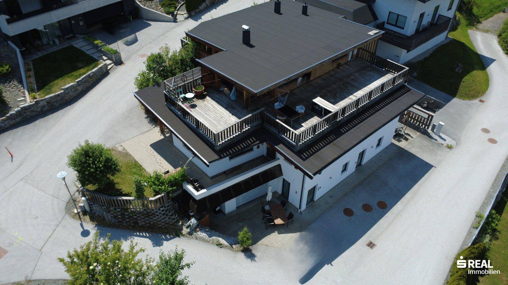 Gesamtansicht des Hauses von oben, mit Terrassen und der umliegenden Wohnbebauung.