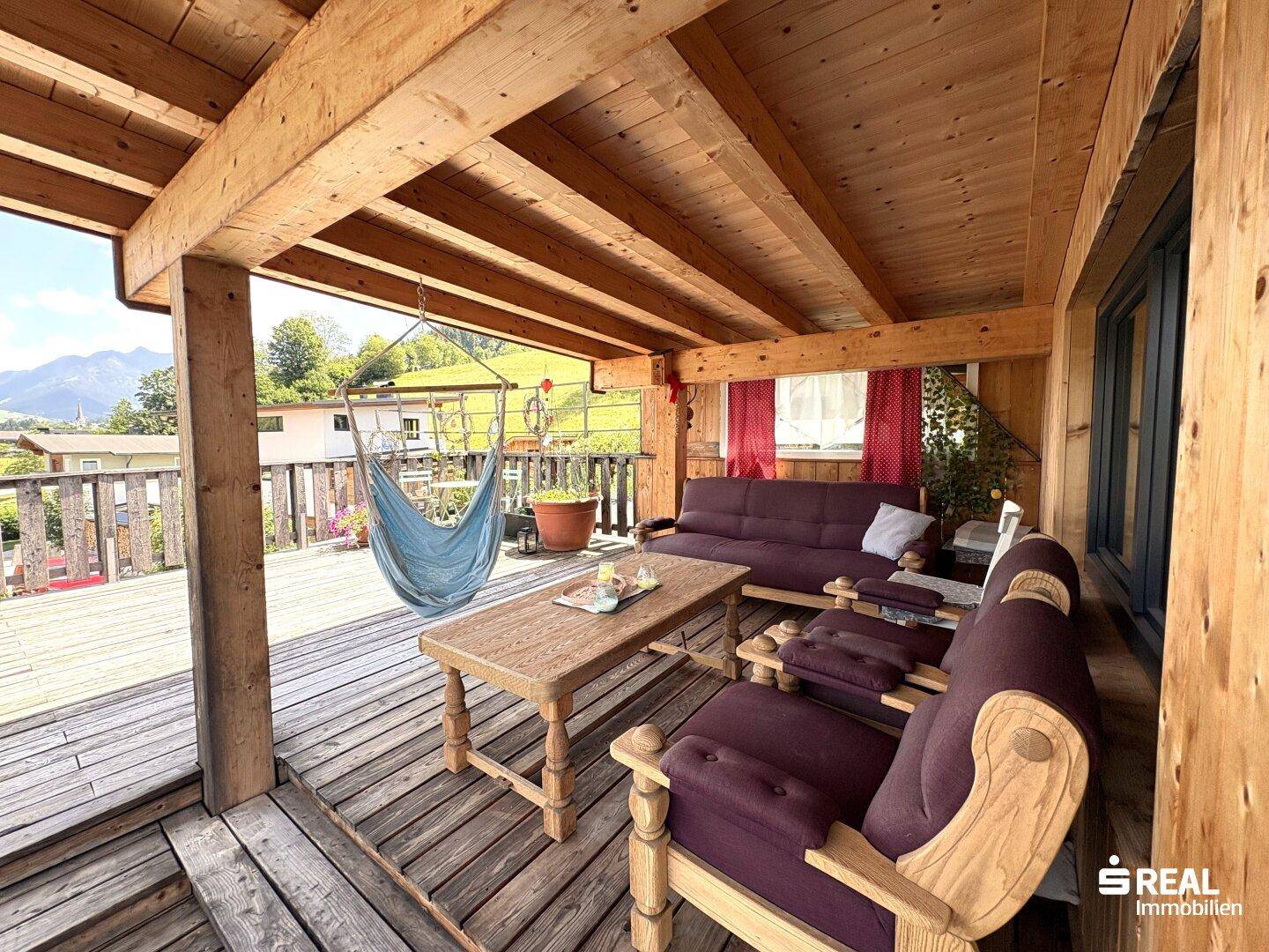 Überdachte Holzterrasse mit bequemen Loungemöbeln und Hängematte für entspannte Stunden.