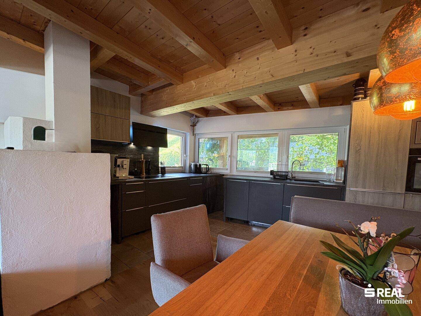 Moderne Wohnküche mit Holzbalkendecke, Fliesenboden und traditionellem Kachelofen.