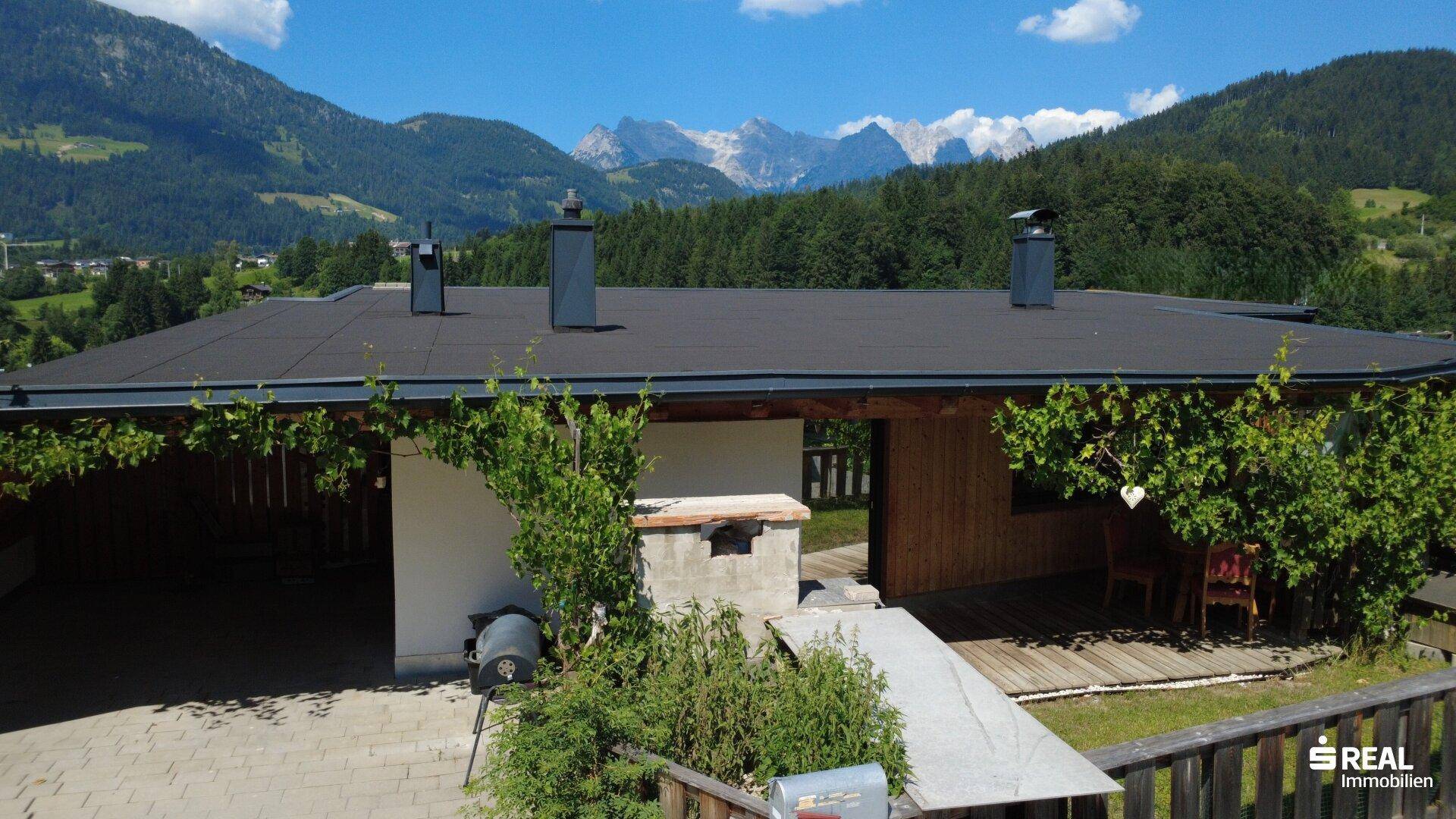 Dachansicht des Hauses mit Flachdach und Schornsteinen vor einer beeindruckenden Bergkulisse.