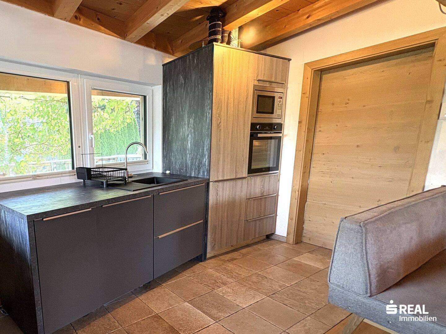 Moderne Einbauküche mit integrierten Geräten, Fliesenboden und Holzbalkendecke.