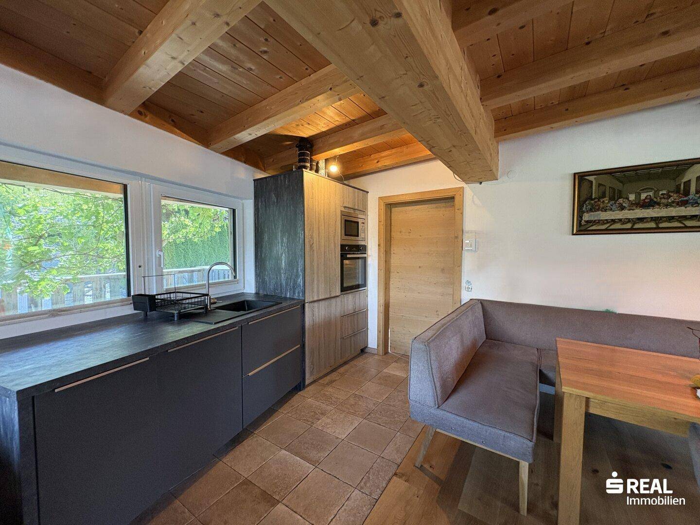 Kompakte Wohnküche mit dunklen Schränken, Fliesenboden und Holzbalkendecke.
