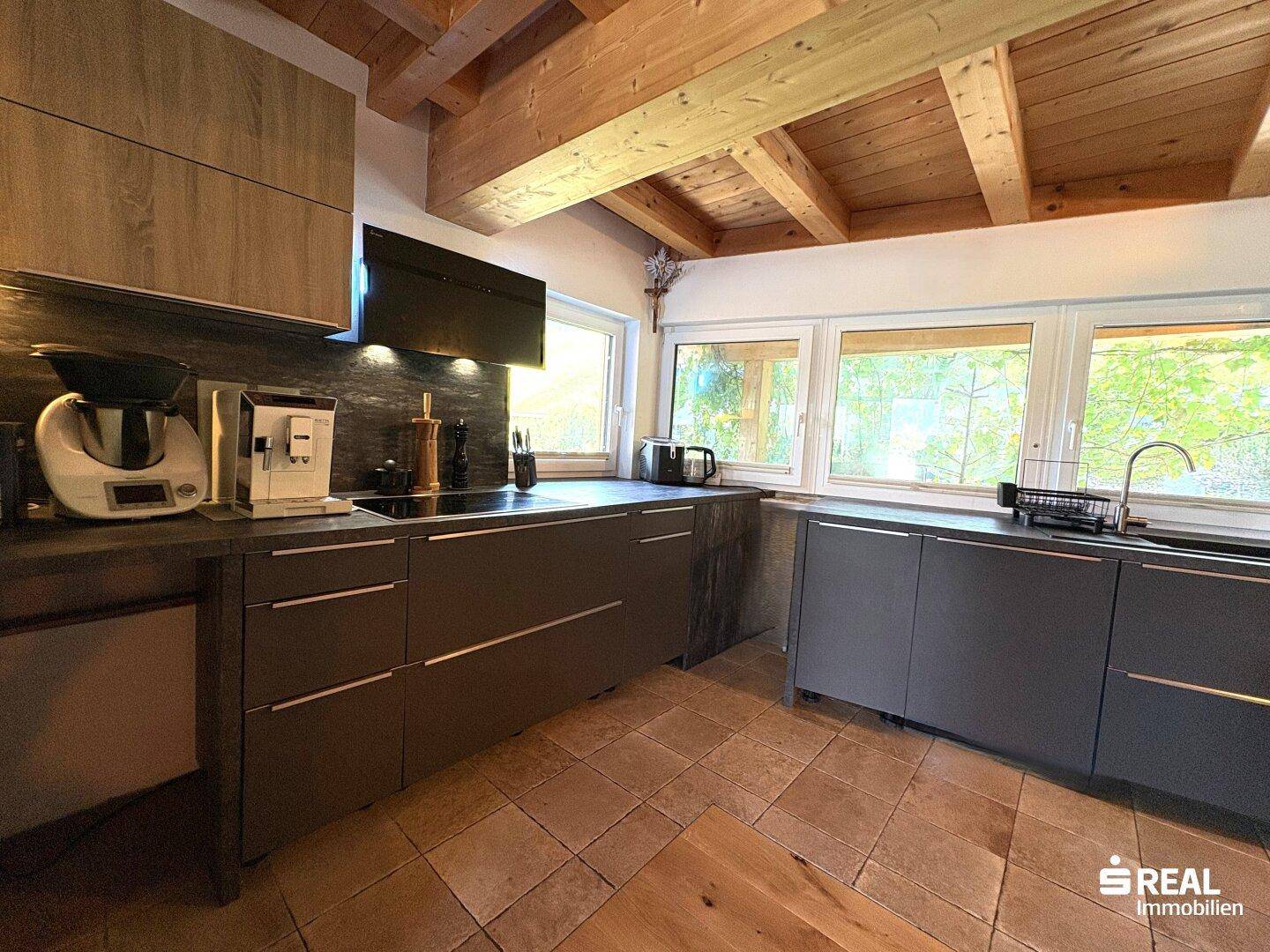 Moderne Küche mit dunklen Fronten, Fliesenboden und Holzbalkendecke.