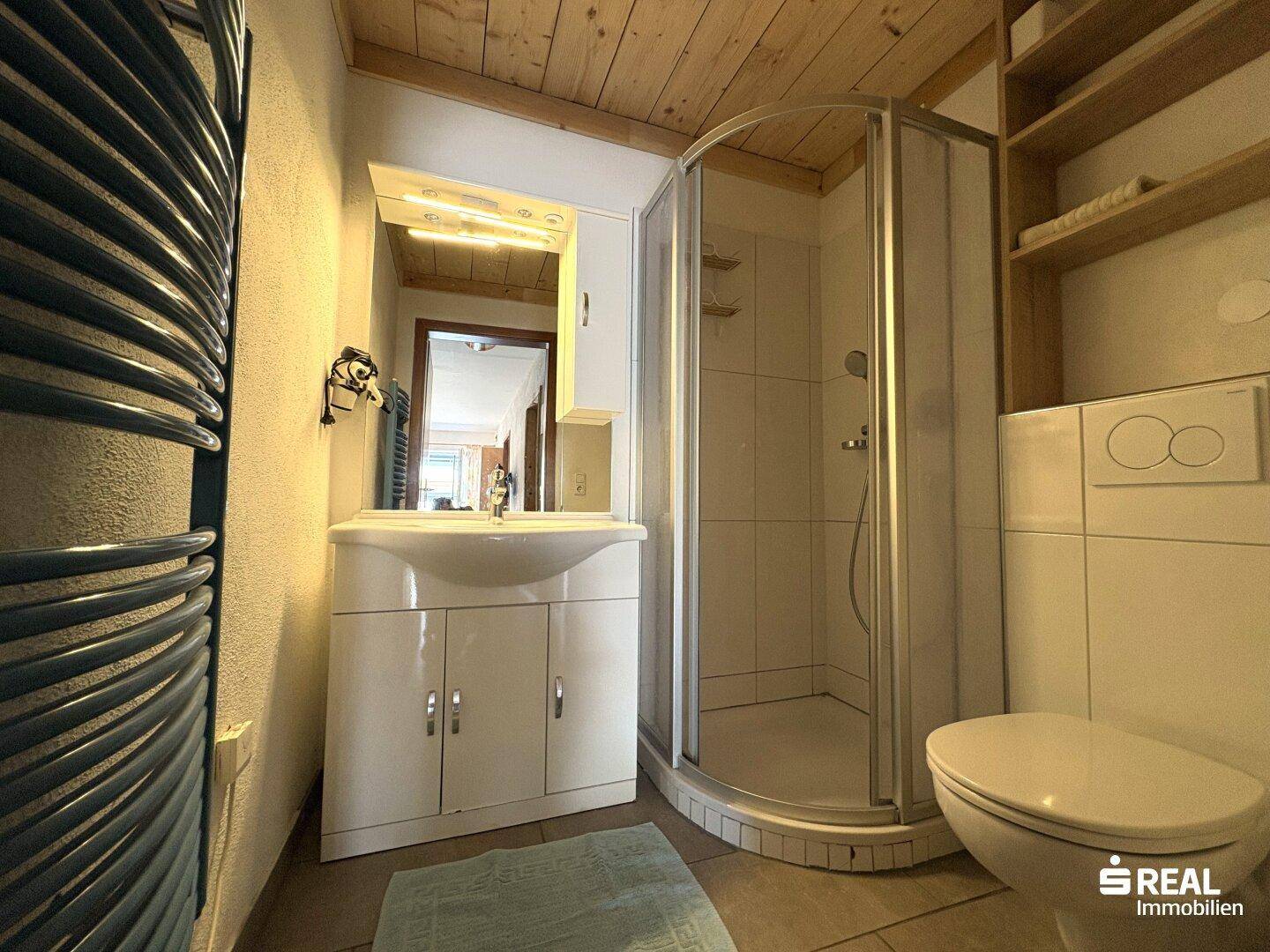 Badezimmer mit Duschkabine, Waschbecken und rustikaler Holzdecke.