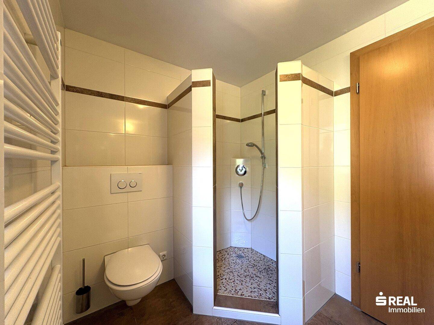 Badezimmer mit gefliester Dusche, wandhängendem WC und beheiztem Handtuchhalter.