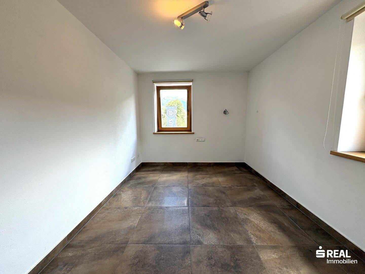 Leeres Zimmer mit Fliesenboden, weiß gestrichenen Wänden und einem Fenster.