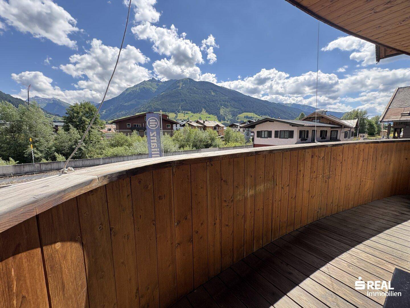 Holzbalkon mit Blick auf die umliegende Berglandschaft unter einem sonnigen Himmel.