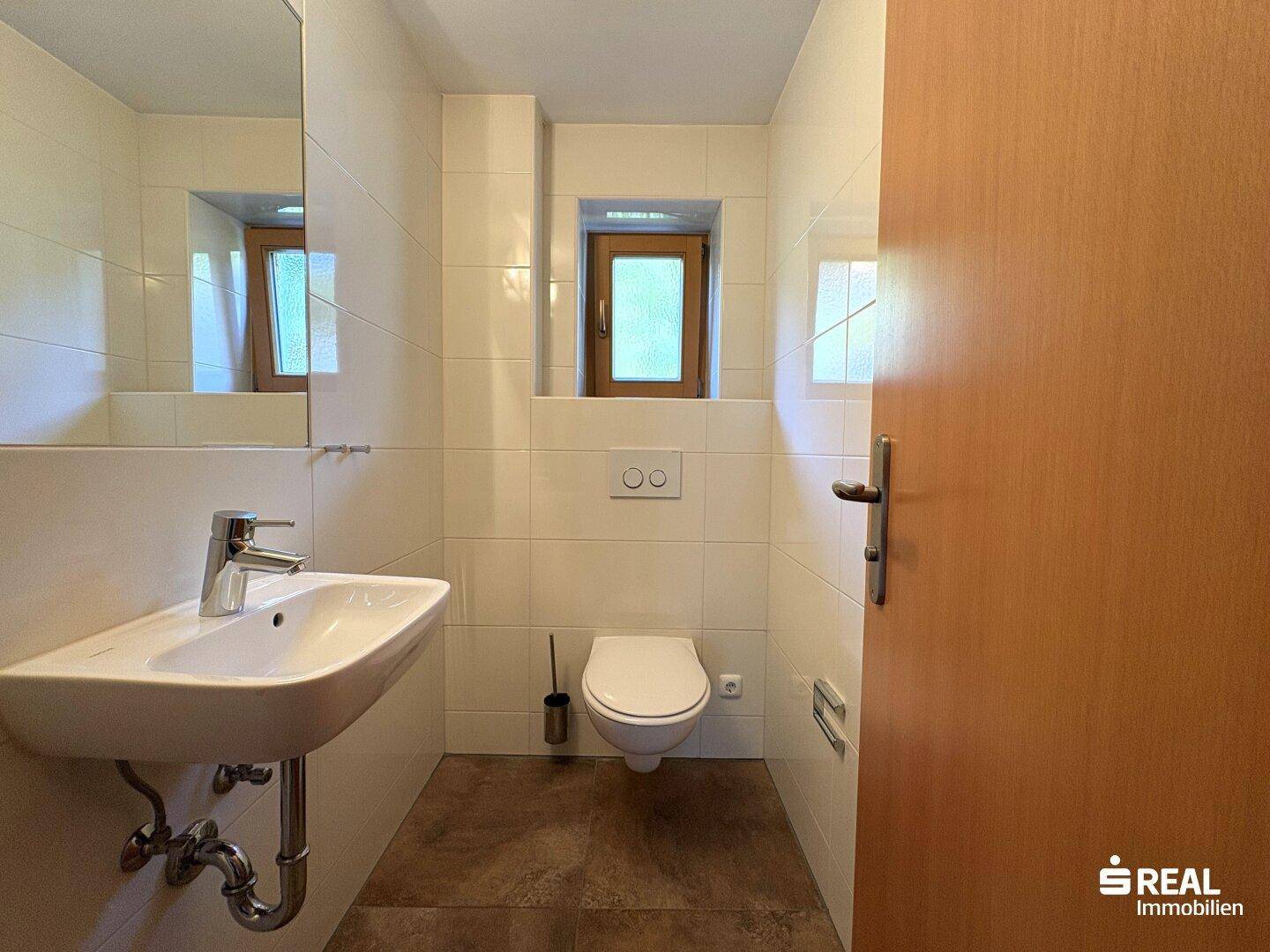 Kleines Badezimmer mit Waschbecken, WC und einem Fenster für natürliche Belüftung.
