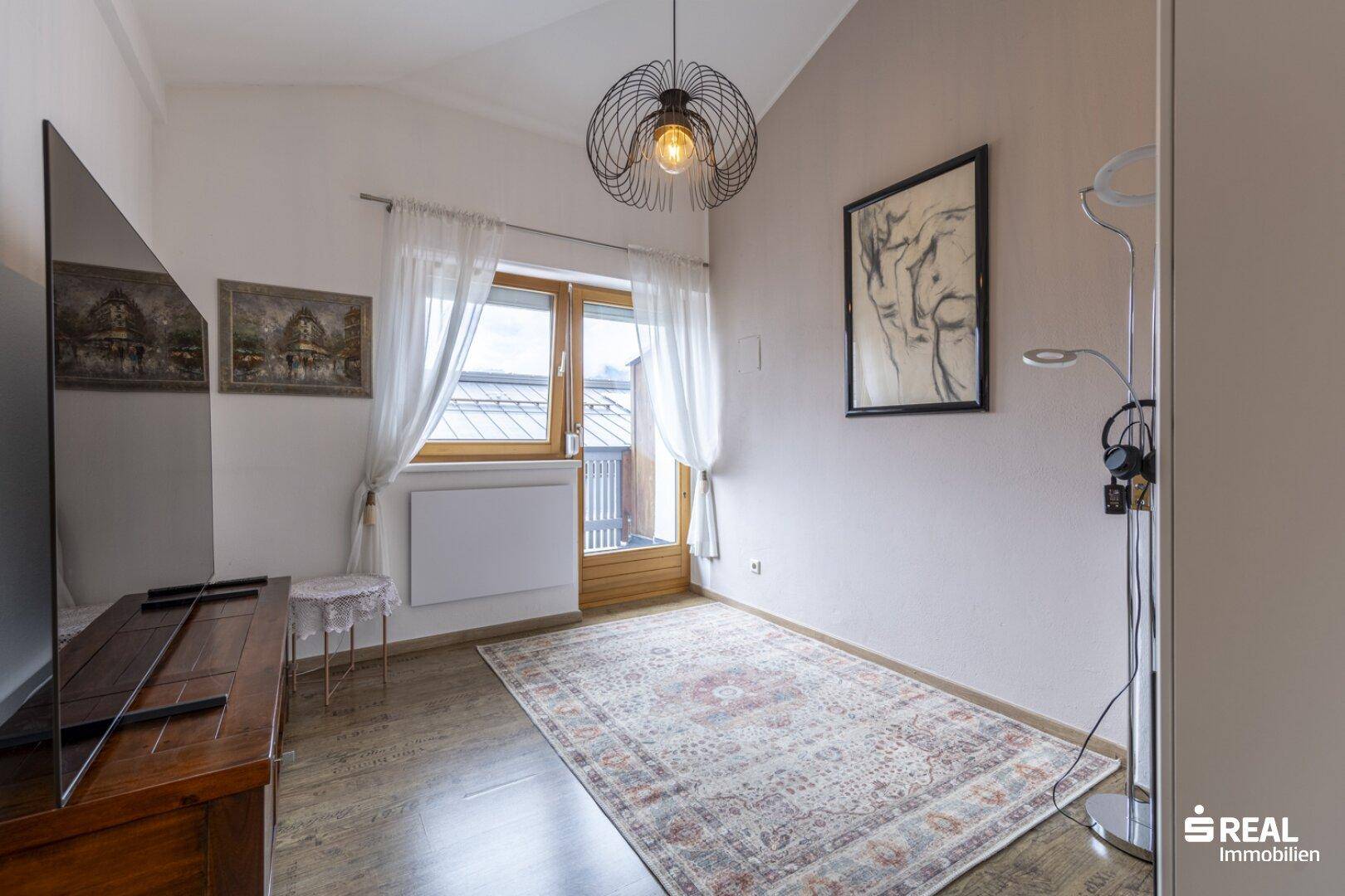 Gemütliches Schlafzimmer mit Holzboden, Dachschräge und Zugang zu einem kleinen Balkon.