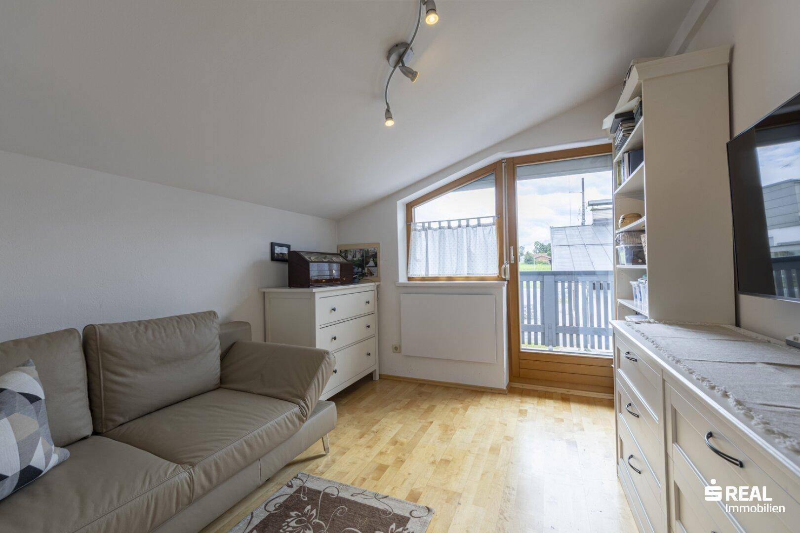 Helles Schlafzimmer mit Holzboden, Dachschräge und Zugang zu einem kleinen Balkon.