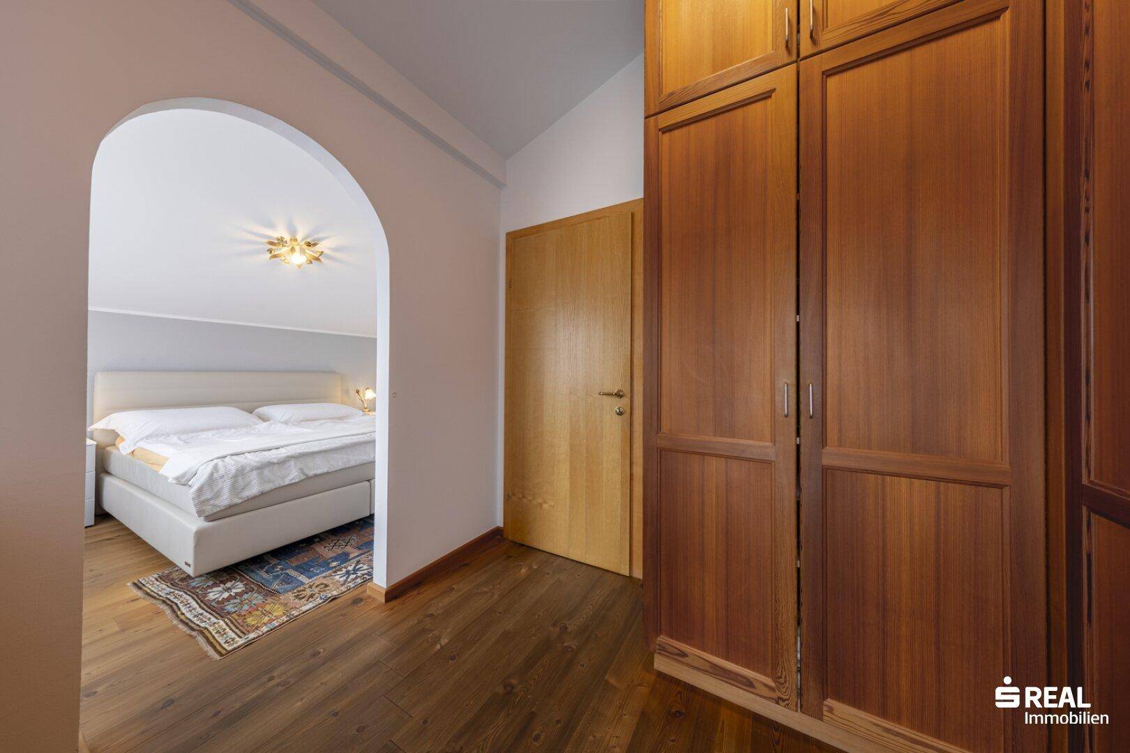 Schlafzimmer mit Holzboden, Einbauschränken und Zugang zu einem weiteren Raum.