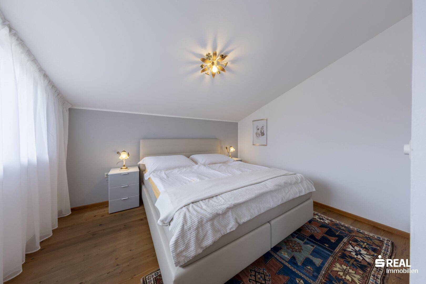 Helles Schlafzimmer mit Doppelbett, Holzboden und Dachschräge.