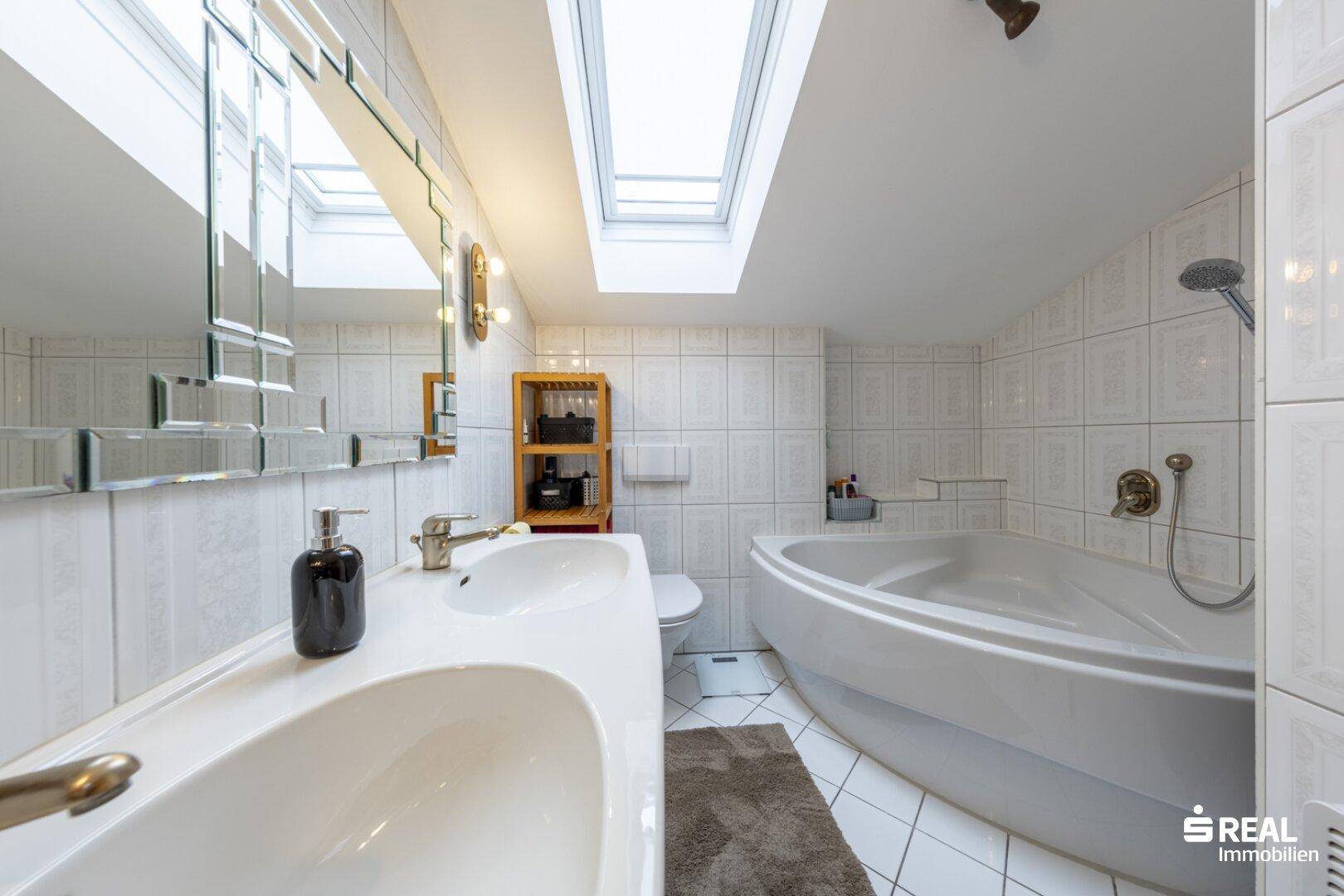 Helles Badezimmer mit Doppelwaschbecken, Eckbadewanne und Dachfenstern für viel Licht.