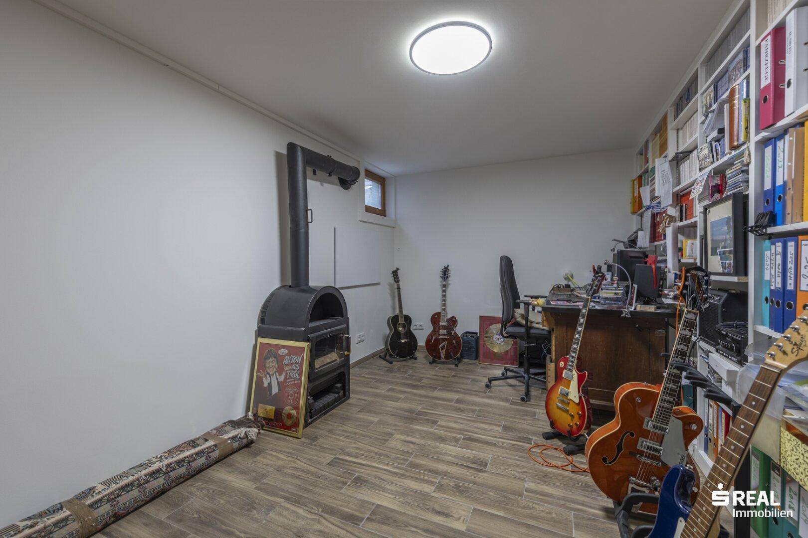 Geräumiger Hobbyraum im Untergeschoss mit Holzofen, Gitarren und Regalen.