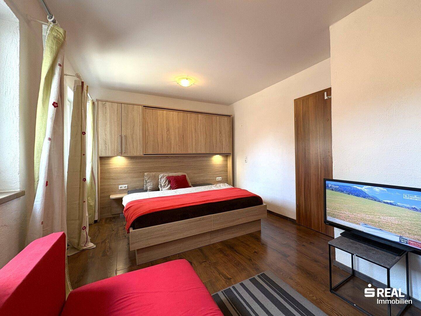 Helles Schlafzimmer mit Holzbett, integrierten Schränken und Fernseher.