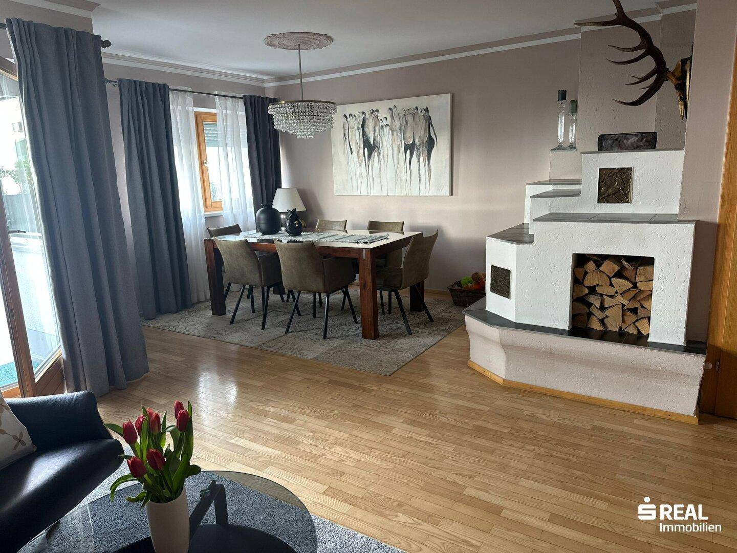 Geräumiger Wohn-Essbereich mit Holzboden, Kachelofen und Zugang zur Terrasse, hell und einladend.