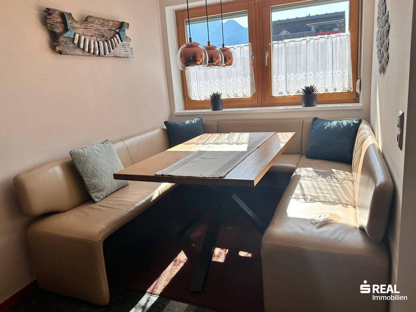 Gemütliche Essecke mit Eckbank, Holztisch und Blick auf die Berge durch das Fenster.
