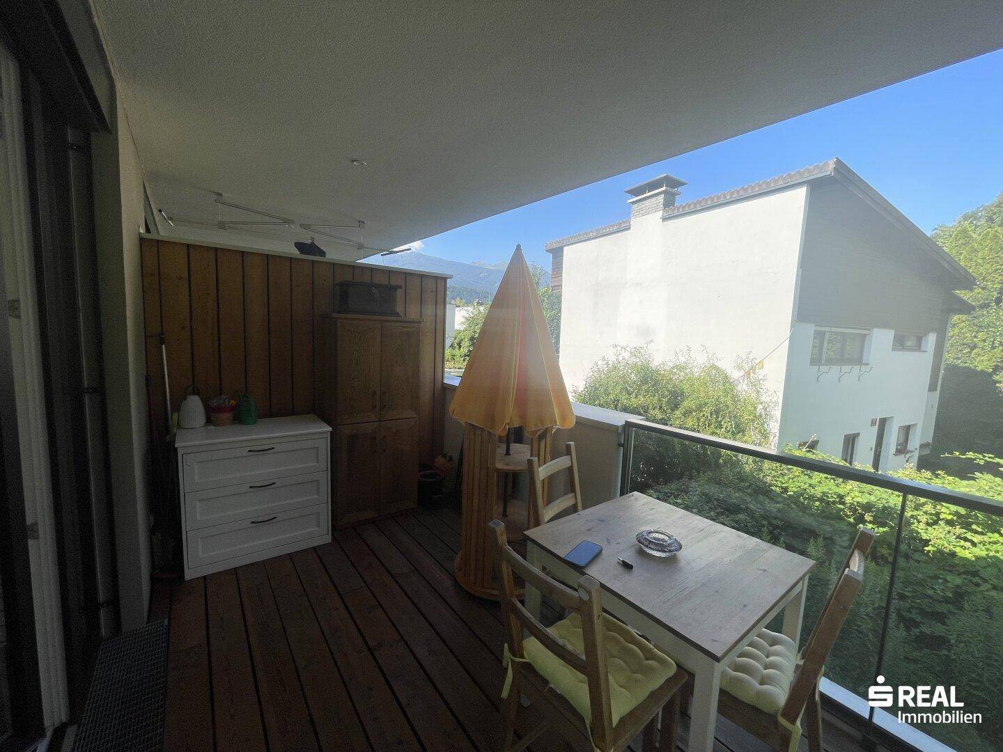 Gemütlicher Balkon mit Holzboden, Sitzgelegenheiten und Blick auf die Umgebung.