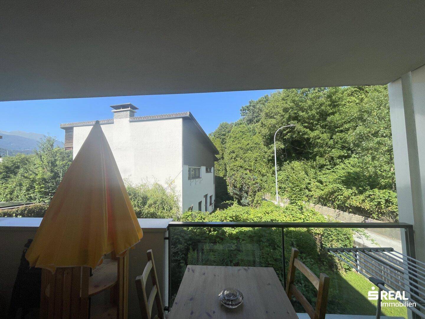 Balkon mit Sitzgelegenheiten und weitem Blick auf die grüne Umgebung und Gebäude.