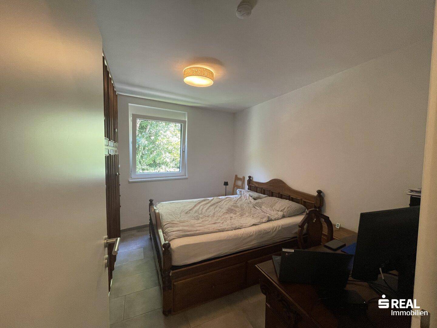 Schlafzimmer mit Holzbett, Schreibtisch und Fenster mit Blick ins Grüne.