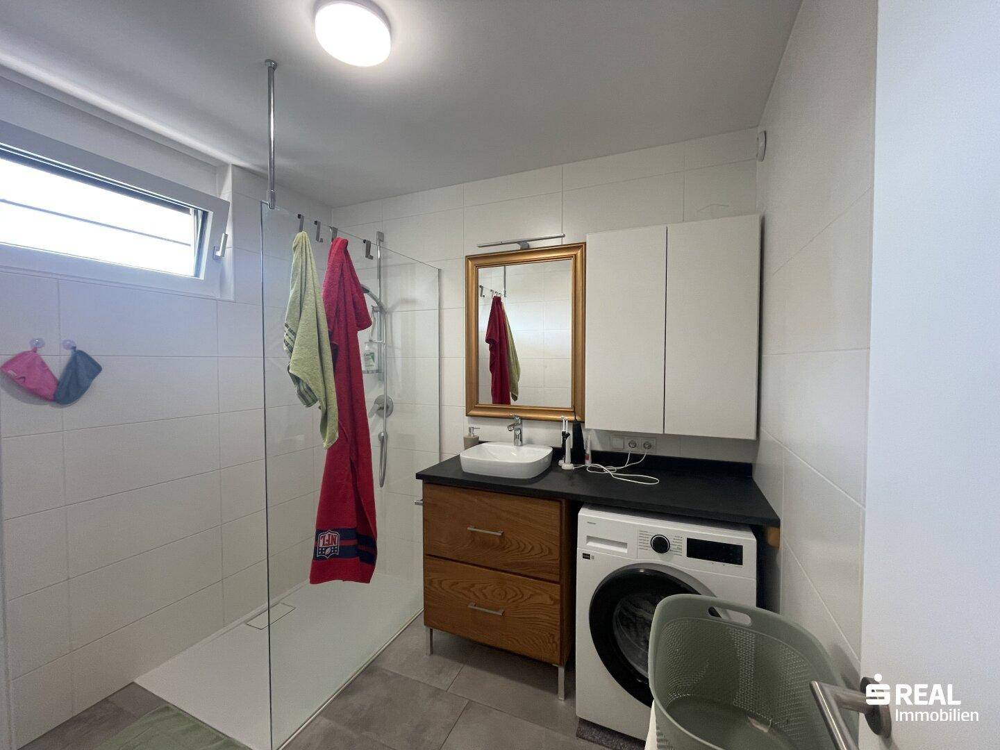 Modernes Badezimmer mit ebenerdiger Dusche, Waschbecken und Waschmaschine.