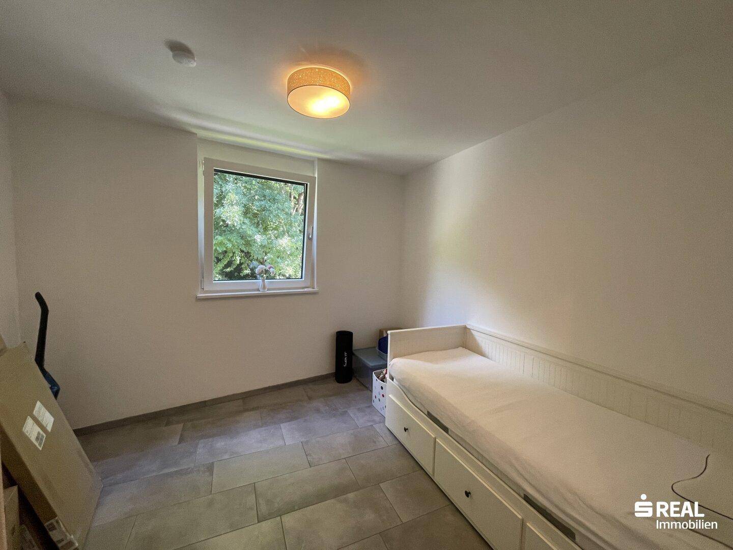 Helles Zimmer mit Einzelbett und Fenster, das viel Tageslicht hereinlässt.