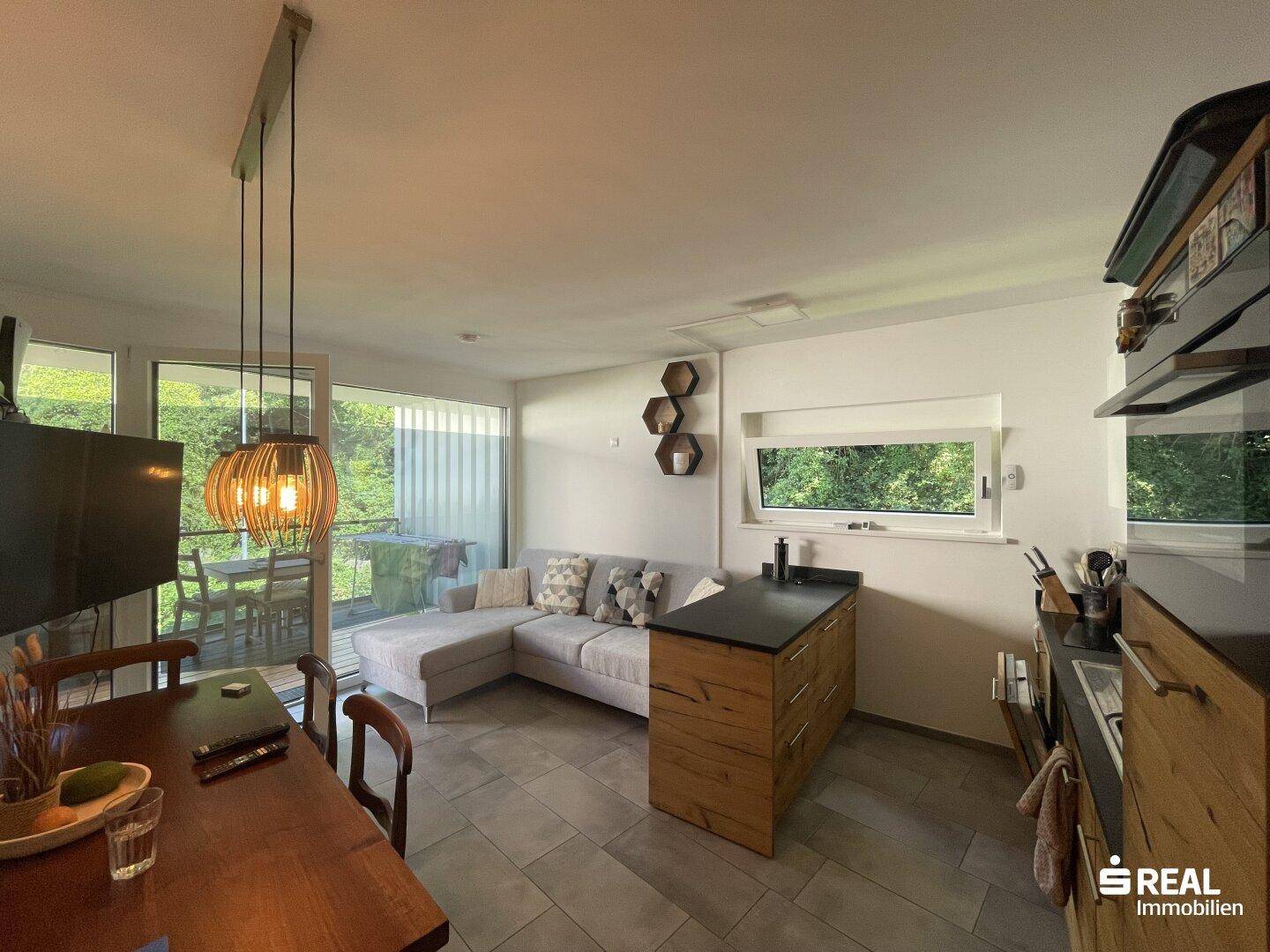 Offener Wohnbereich mit Essplatz, integrierter Küche und Zugang zum Balkon.