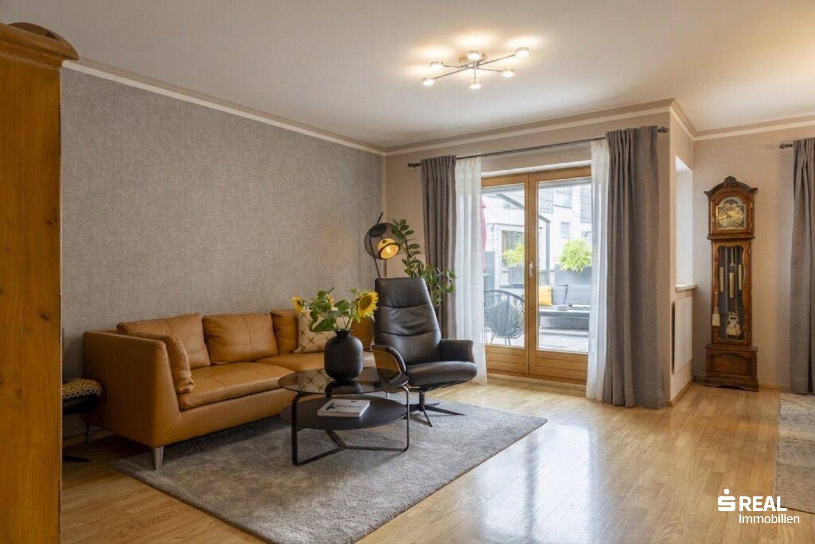 Gemütliches Wohnzimmer mit Ledersofa, Holzboden und großem Fenster zur Terrasse.