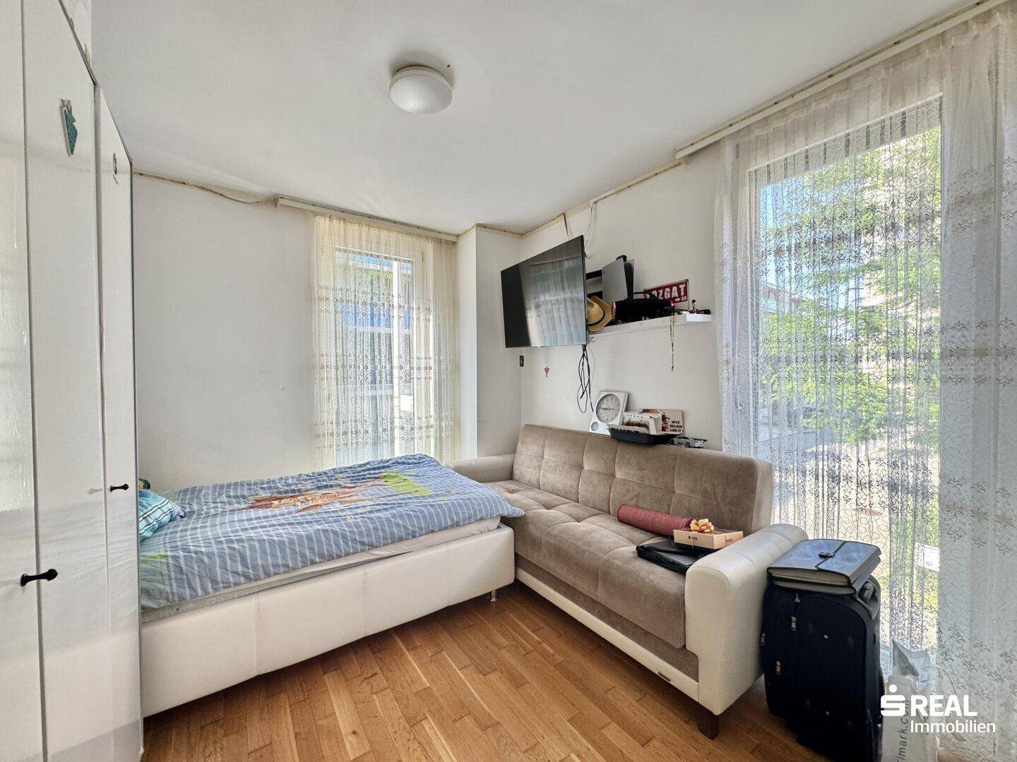 Helles Schlafzimmer mit Einzelbett, Sofa und großem Fenster.