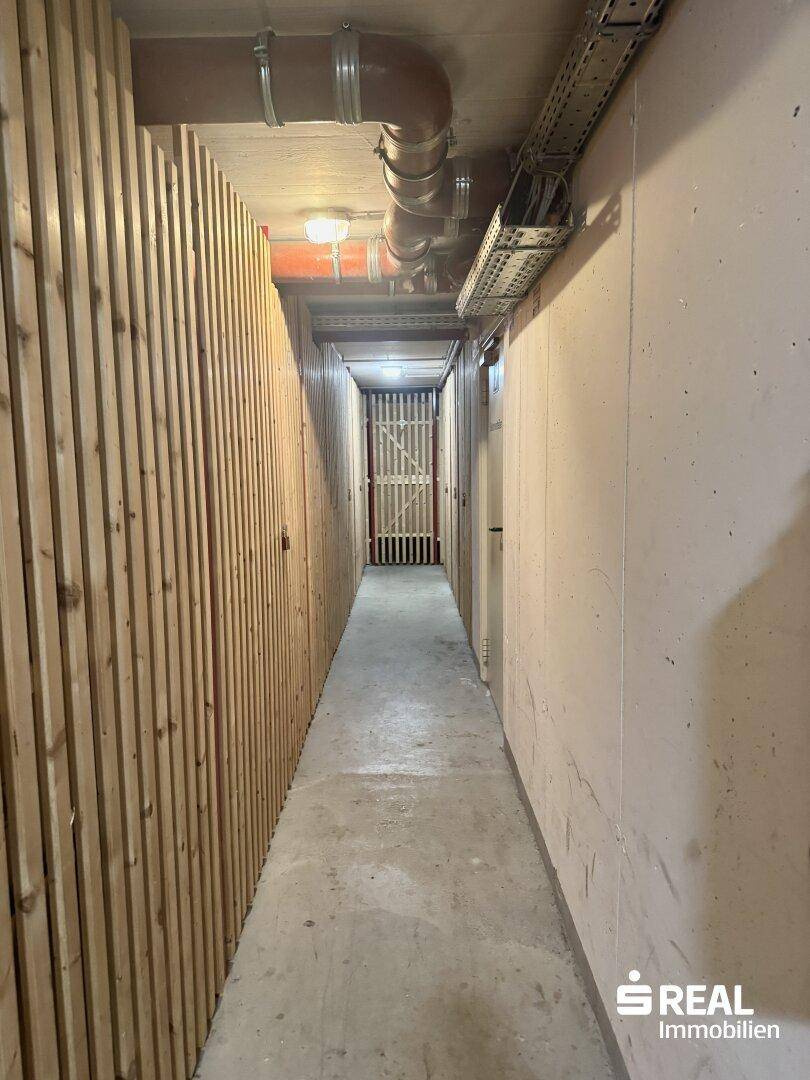 Langer Kellergang mit Holzverschlägen und Betonboden.