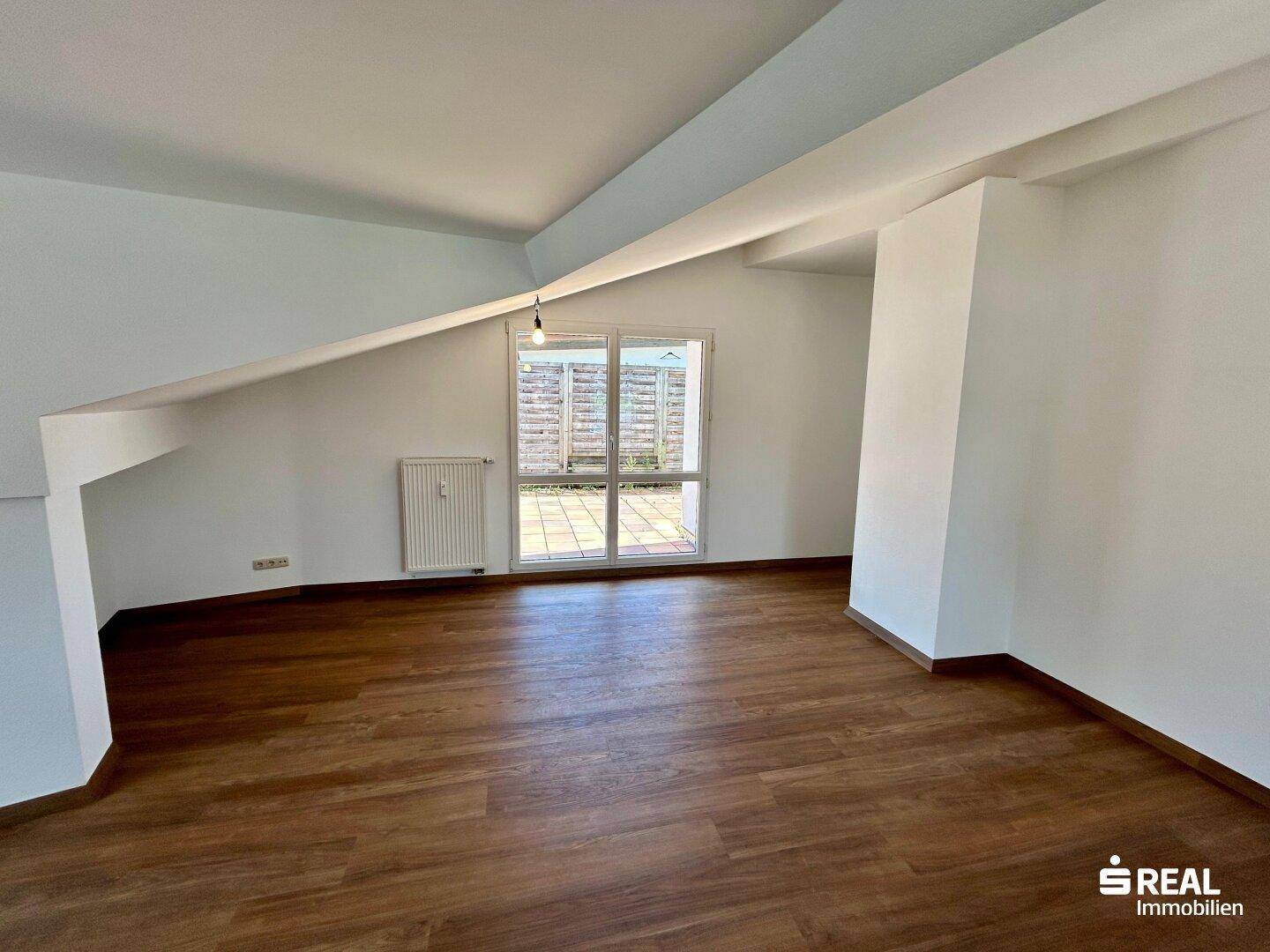 Heller Wohnraum mit Laminatboden und großen Fenstern, die viel Tageslicht hereinlassen.