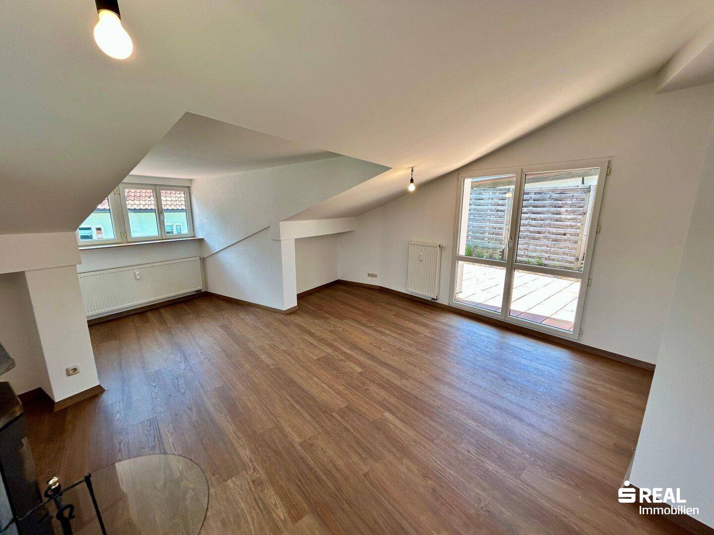 Geräumiger Wohnbereich im Dachgeschoss mit Laminatboden, schrägen Decken und Zugang zur Terrasse.