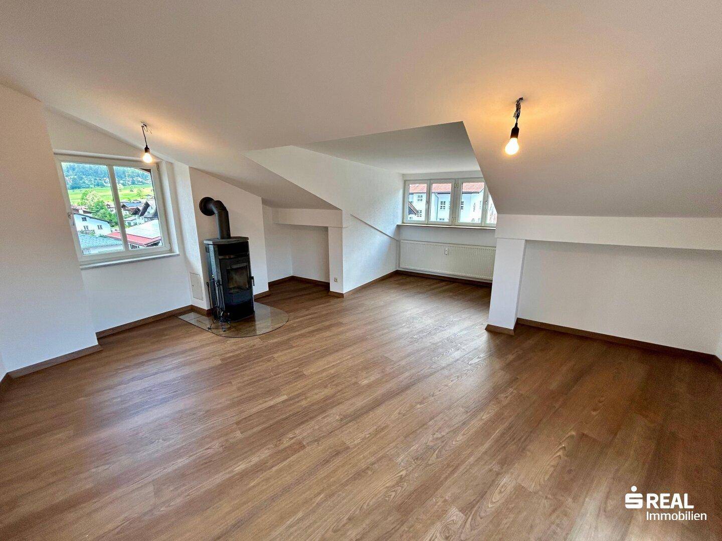 Heller Wohnraum im Dachgeschoss mit Laminatboden, Kaminofen und Fenstern mit Ausblick.