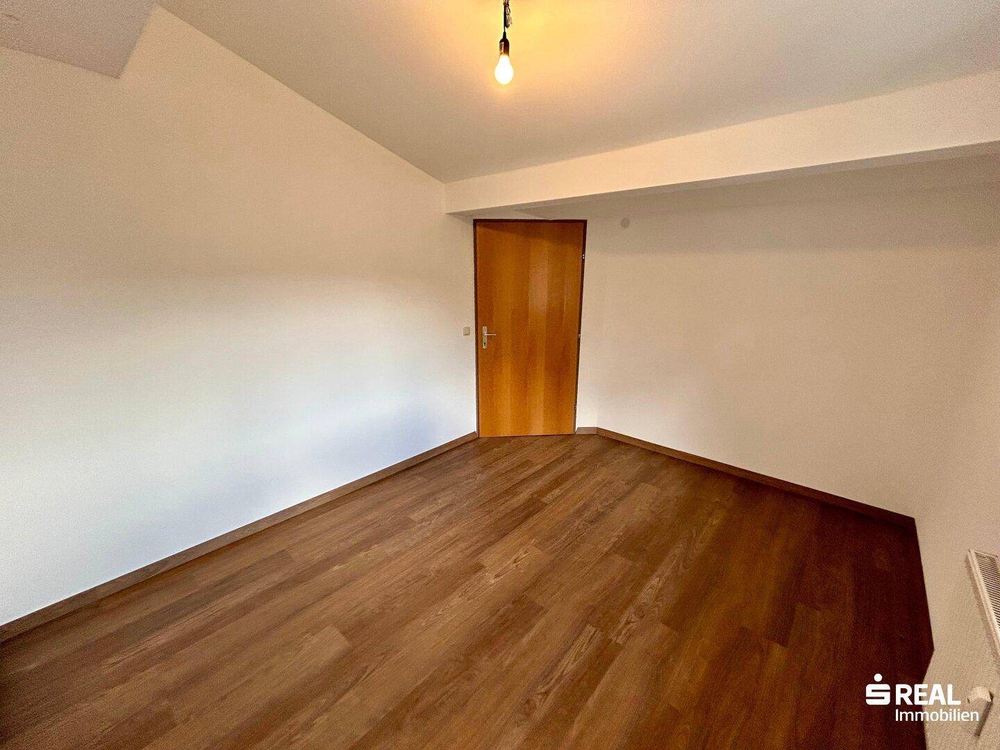 Einfaches Schlafzimmer mit Laminatboden und einer Holztür, bereit zur individuellen Gestaltung.