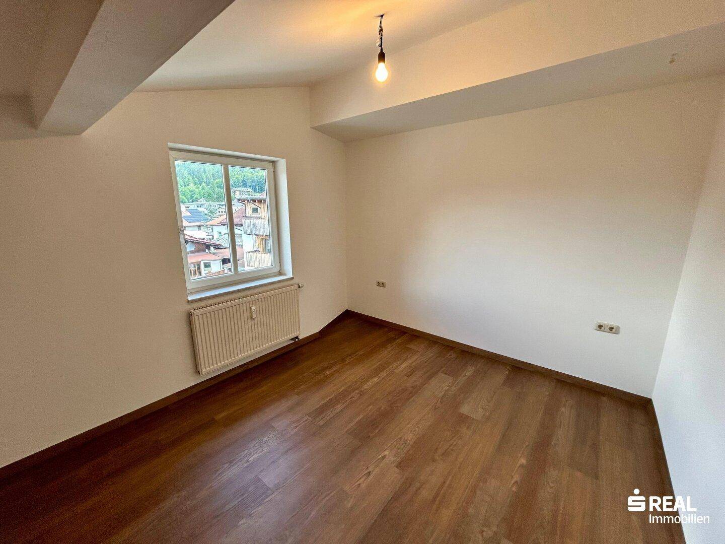 Kleines Schlafzimmer mit Laminatboden und einem Fenster mit Blick auf die Umgebung.