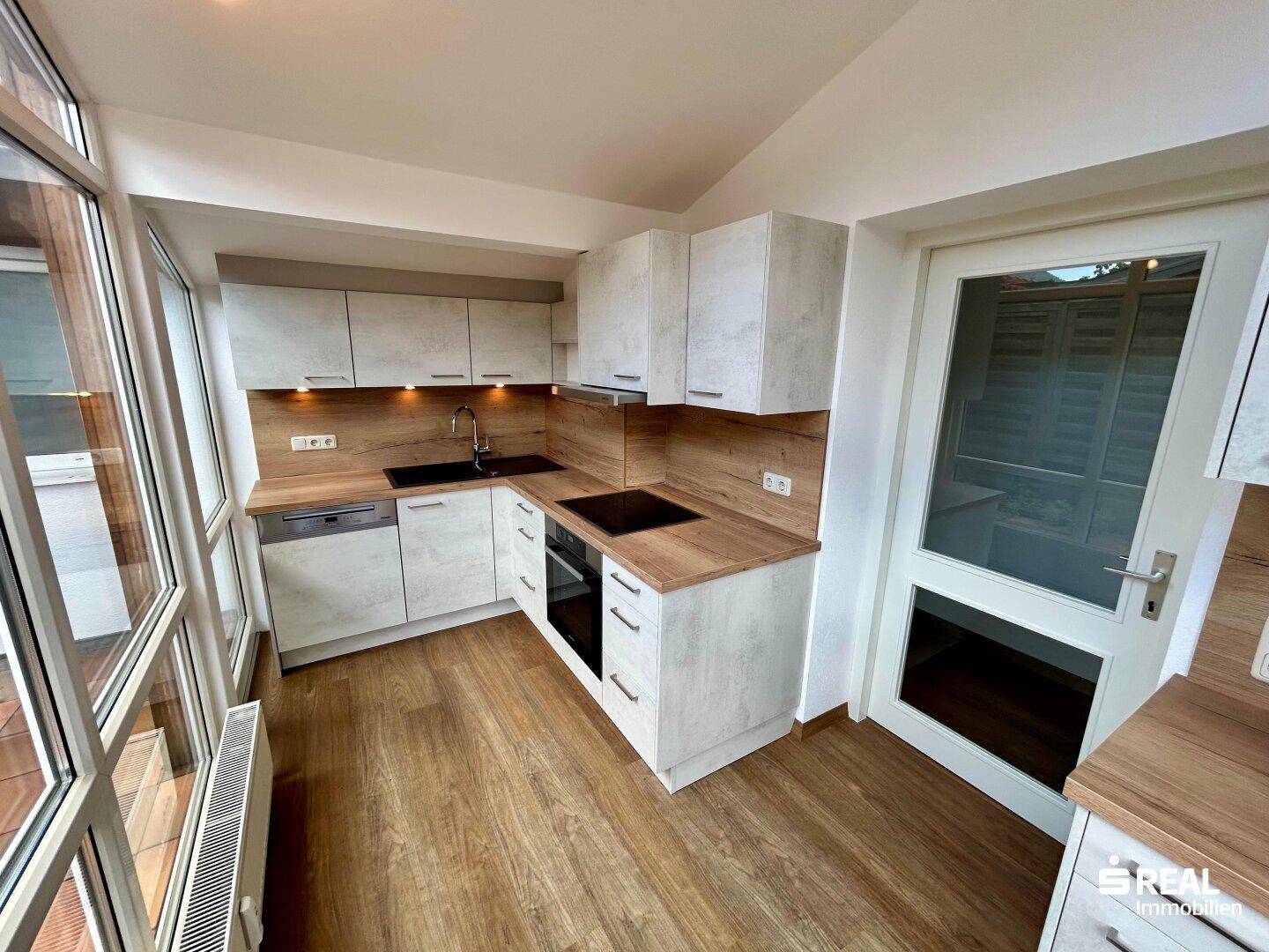 Moderne Einbauküche mit hellen Schränken, Holzarbeitsplatten und Zugang zur Terrasse.
