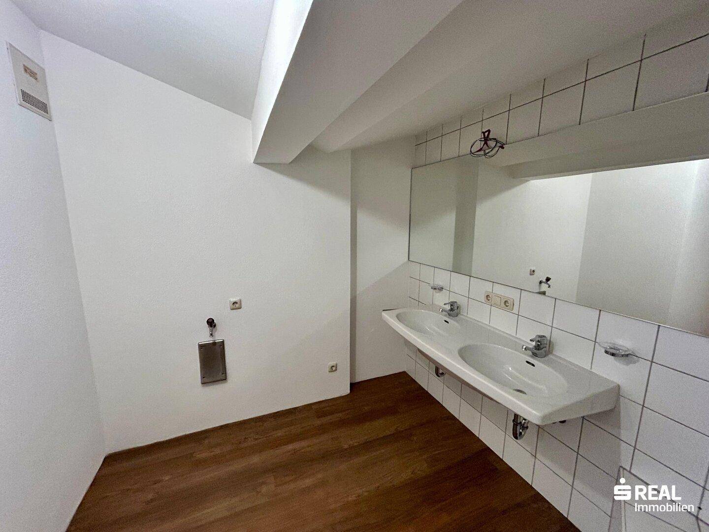 Geräumiges Badezimmer mit Doppelwaschbecken, großem Spiegel und weißen Fliesen.