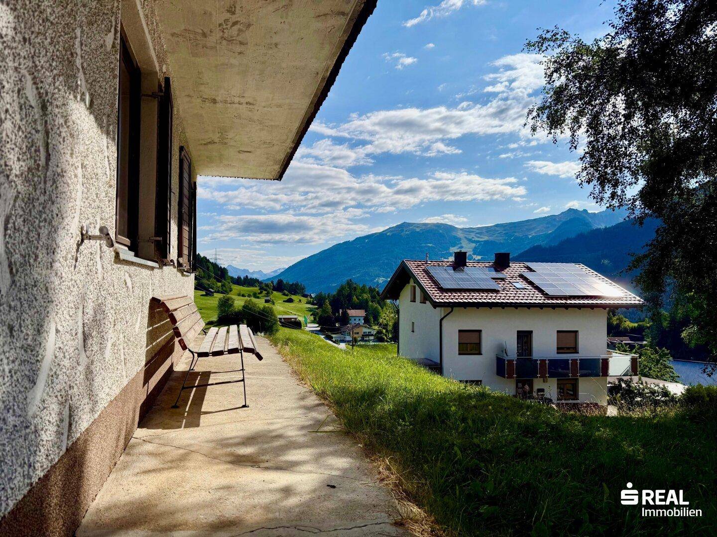Seitenansicht des Hauses mit einer Holzbank und Panoramablick auf die Berge und das Tal.