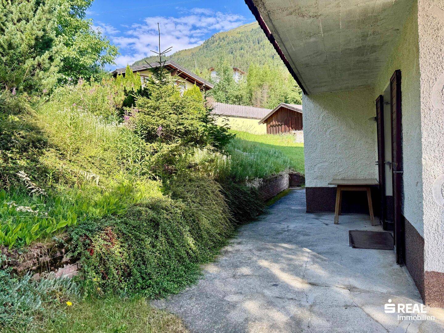 Außenbereich des Hauses mit einem gepflasterten Weg und üppiger grüner Bepflanzung.